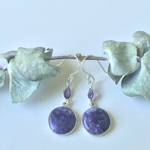 May include: A pair of silver dangle earrings with a round purple stone and a teardrop-shaped purple stone on each earring.