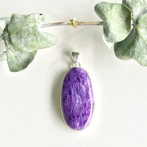May include: A silver pendant featuring a large, oval-shaped purple gemstone. The gemstone has a shimmering, iridescent quality.