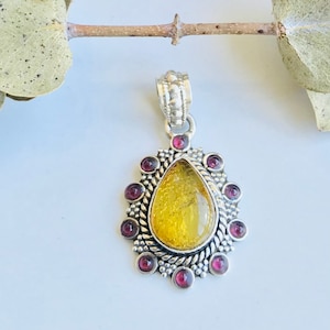 May include: A silver pendant featuring a teardrop-shaped yellow gemstone set within a silver frame adorned with small purple gemstones.