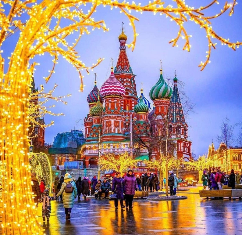 May include: A colorful, ornate building with multiple onion domes and a red brick facade. The building is decorated with intricate details and is surrounded by a festive atmosphere. The building is lit up with lights and there are people walking around in front of it.