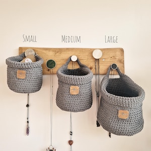 3 dark grey hanging crochet baskets with a vegan friendly cork "woolflower" logo. Great for bedrooms, bathrooms and nursery home organisation on Etsy!