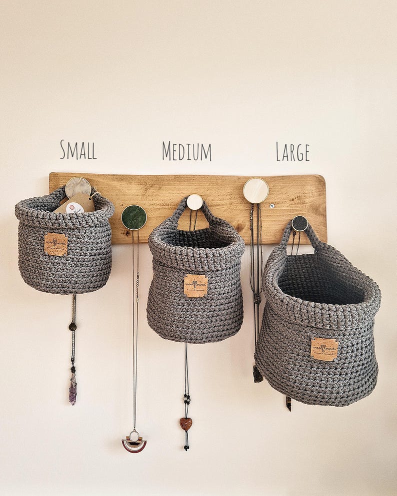3 dark grey hanging crochet baskets with a vegan friendly cork "woolflower" logo. Great for bedrooms, bathrooms and nursery home organisation on Etsy!