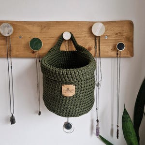 An olive green cotton crochet hanging basket with a vegan friendly cork "woolflower" logo. Great for bedrooms, bathrooms and nursery for storing toiletries, make-up, vitamins, pegs, etc. Natural home organisation on Etsy by Woolflowerdesigns!