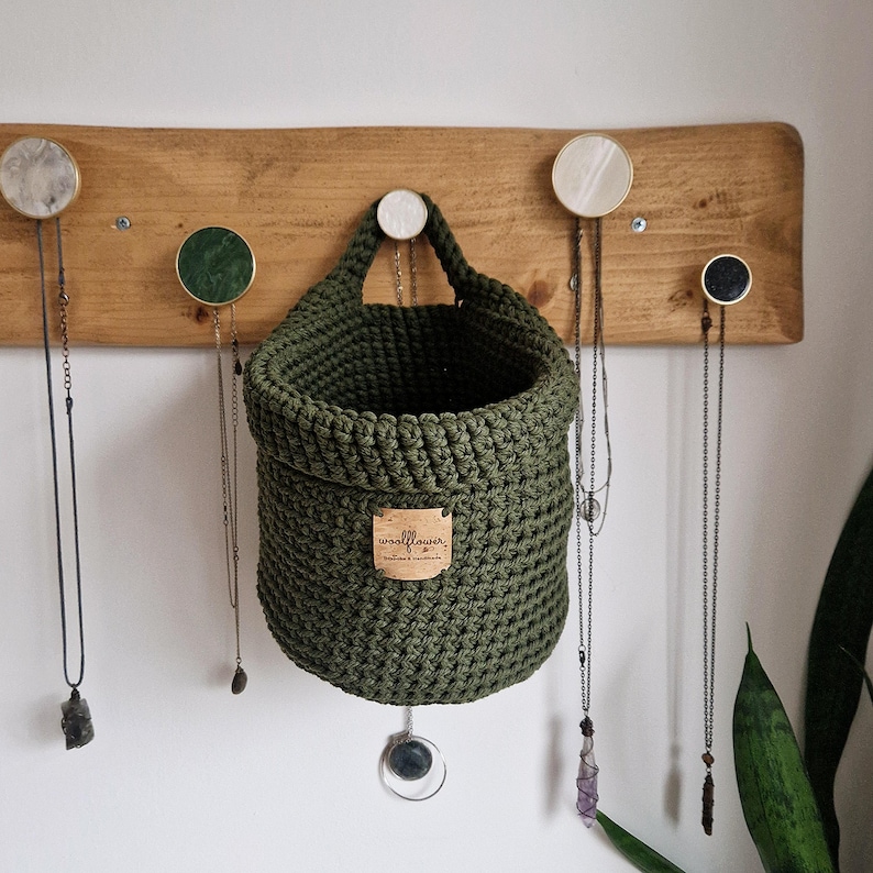 An olive green cotton crochet hanging basket with a vegan friendly cork "woolflower" logo. Great for bedrooms, bathrooms and nursery for storing toiletries, make-up, vitamins, pegs, etc. Natural home organisation on Etsy by Woolflowerdesigns!