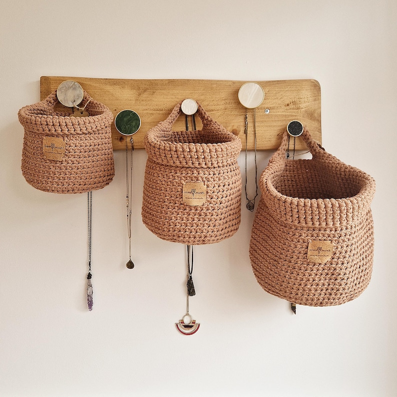 3 light brown hanging crochet baskets with a vegan friendly cork "woolflower" logo. Great for bedrooms, bathrooms and nursery home organisation on Etsy by Woolflowerdesigns!