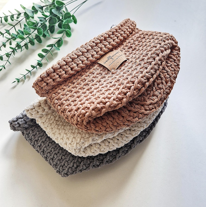 Three crocheted baskets stacked on top of each other. The top basket is slamon brown, the middle basket is off white, and the bottom basket is grey. The top basket has a brown label with the text "woolflower" on it.