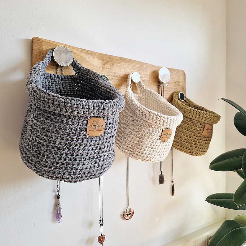 3 crochet cotton storage baskets hang against a natural wooden shelf on Etsy. The dark grey is large sized, natural is mecium and light green is  small. The storage baskets are vegan friendly. Perfect for home organisation!