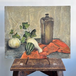 May include: An oil painting on canvas depicting a still life with a tall dark bottle, a round pale melon, a striped green gourd, and a white squash. Green ivy leaves are intertwined among the produce, all resting on a bright orange cloth.