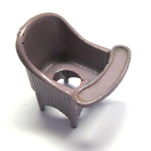 May include: A vintage, lavender-colored toy bathtub with a curved back and a small, attached armrest. The tub has a ribbed exterior and sits on three small legs. The paint shows signs of wear, adding to its antique charm.