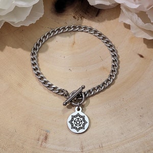 Può includere: Un braccialetto a catena d'argento con una chiusura a scorrimento in argento e un ciondolo d'argento con un design a pentacolo.