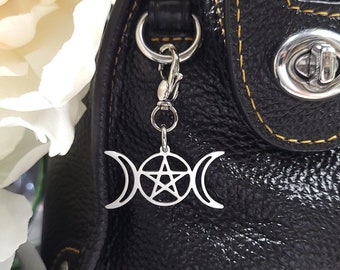 May include: A black leather handbag with a silver charm attached to the zipper pull. The charm features a pentacle and triple moon symbol.