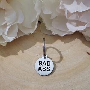 May include: Silver keychain with a round tag that says "BAD ASS" in black lettering.