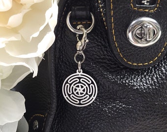 May include: A black leather handbag with a zipper closure and a silver charm attached to the zipper pull. The charm is a circular design with a star in the center.