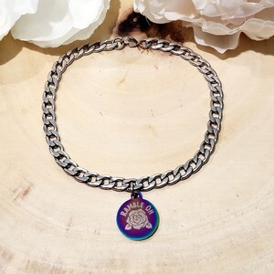 May include: A silver chain necklace with a round charm that says "ramble on" with a rose design. The charm has a rainbow iridescent finish.