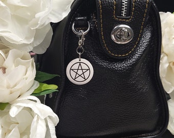 May include: A black leather satchel bag with a yellow stitch detail and a silver zipper. The bag has a silver clasp and a silver charm with a pentagram design.