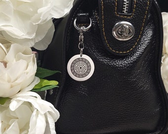 May include: Black leather handbag with a yellow stitch detail and a silver zipper. The bag has a silver clasp and a silver charm with a circular design.