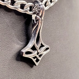 May include: A silver chain necklace with a detailed silver pendant in the shape of a stylised hammer.