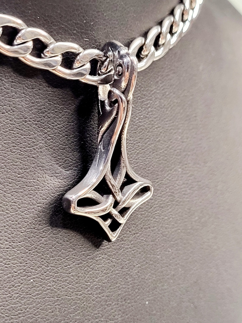 May include: A silver chain necklace with a detailed silver pendant in the shape of a stylised hammer.