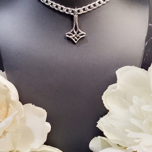 May include: A silver chain necklace with a geometric pendant. The pendant is a stylised diamond shape with a knot design.