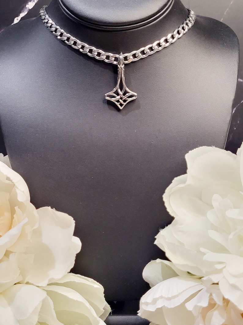 May include: A silver chain necklace with a geometric pendant. The pendant is a stylised diamond shape with a knot design.