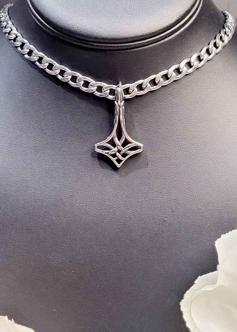 May include: A silver chain necklace with a silver pendant featuring a geometric design. The pendant is shaped like a diamond with intricate details.