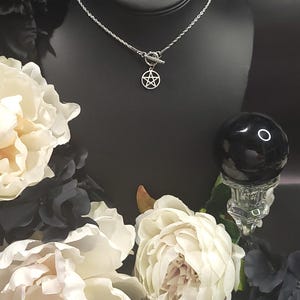 Op de afbeelding: Een zilveren ketting met een zilveren toggle-sluiting en een zilveren pentagram-hanger. De ketting wordt getoond op een zwarte mannequin-buste.