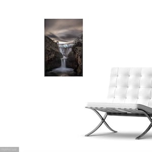 May include: A dramatic black and white photograph of a waterfall cascading down a rocky cliff face. The water is blurred, creating a sense of motion. The sky above is cloudy and dark.