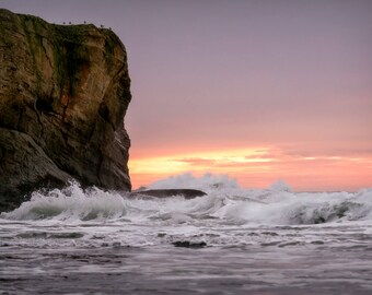 May include: A rocky cliff juts out into the ocean, with crashing waves in the foreground. The sky is a vibrant pink and orange, creating a dramatic sunset scene.