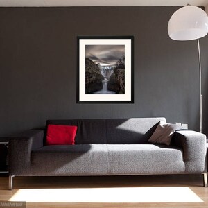 May include: A framed photograph of a waterfall cascading down a rocky cliff. The photo is in a black frame and is hanging on a gray wall in a living room setting.