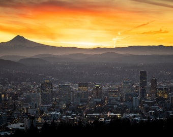 May include: A panoramic view of a city skyline at sunrise with a snow-capped mountain in the background. The city is illuminated by the golden light of the rising sun, and the mountain is silhouetted against the orange and yellow sky.