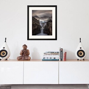 May include: A framed photograph of a waterfall cascading down a rocky cliff. The sky is overcast and the scene is dramatic.