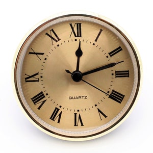 May include: A gold-colored round clock with Roman numeral markings and a black face. The clock reads "QUARTZ" and has black hands.