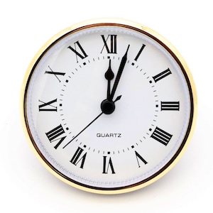 May include: A white clock face with black Roman numeral hour markers and black hands. The clock face is surrounded by a gold-colored frame. The clock face reads "QUARTZ".