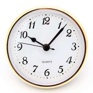 May include: A white clock face with black numbers and hands, surrounded by a gold-colored frame. The clock face reads "QUARTZ" and has a black hour hand pointing to the 1 and a black minute hand pointing to the 12.