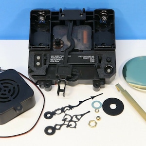 May include: A black clock kit with a chime mechanism, two black hands, a gold pendulum, a black speaker, and a gold-colored face. The clock kit includes instructions for assembling the clock.