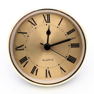 May include: A gold-colored round clock with Roman numeral markings and a black face. The clock reads "QUARTZ" and has black hands.