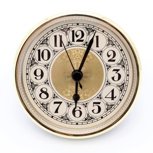 May include: A gold-toned clock face with black Roman numeral hour markers and black hands. The clock face has a decorative pattern and a gold-toned outer ring.