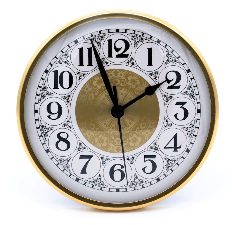 May include: A gold-framed clock with black hands and Roman numeral markings on a white face. The clock face has a decorative gold center with a floral pattern.