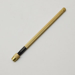 May include: A gold-colored metal drill bit holder with a black grip. The holder is about 6 inches long.