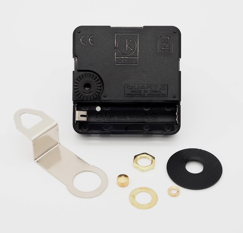 Puede incluir: Un mecanismo de reloj de cuarzo negro con un soporte de metal plateado y varias piezas peque&ntilde;as de hardware de lat&oacute;n y doradas. El mecanismo del reloj tiene un compartimento para pilas y est&aacute; marcado "QUARTZ MADE IN CHINA".