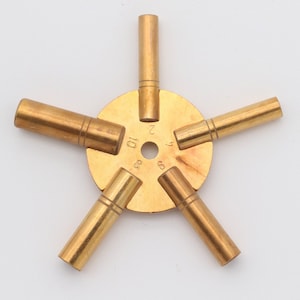 May include: A brass key winding tool with five different sized keys attached to a central disc. The disc is marked with numbers 1, 2, 3, 4, 5, 6, 8, 10.