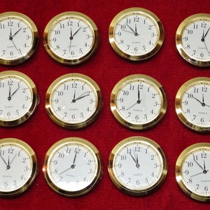 May include: Ten gold-colored round analog clocks with white faces and black hands. Each clock has black numbers and the word "QUARTZ" printed on the face.