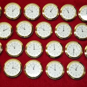 May include: A collection of quartz clock inserts with gold-colored bezels and white faces. The clocks have black numerals and hands, with the time displayed at various positions. The background is a solid red.