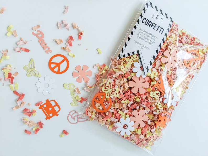 May include: A clear plastic bag filled with colorful confetti featuring peace signs, flowers, and the words "Peace" and "Groovy". The bag has a white tag with the text "CONFETTI" and instructions for using the confetti.