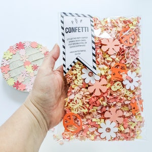May include: A clear plastic bag filled with confetti. The confetti is a mix of orange, yellow, and pink paper. The bag has a tag attached to it that says "CONFETTI" and "Let's get this party started! Sprinkle inside cards, stuff into balloons, or scatter everywhere! Handmade parties on Etsy."