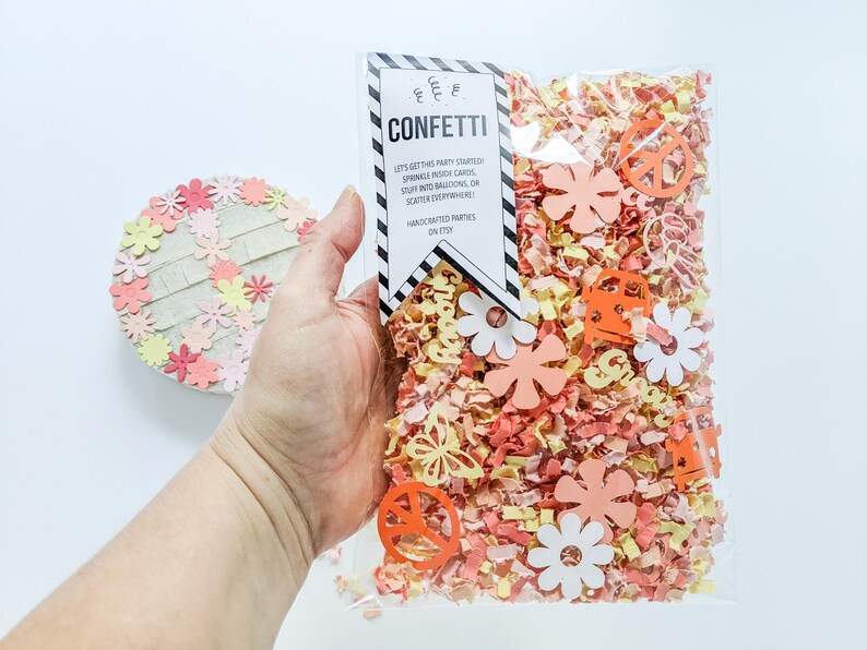 May include: A clear plastic bag filled with confetti. The confetti is a mix of orange, yellow, and pink paper. The bag has a tag attached to it that says "CONFETTI" and "Let's get this party started! Sprinkle inside cards, stuff into balloons, or scatter everywhere! Handmade parties on Etsy."