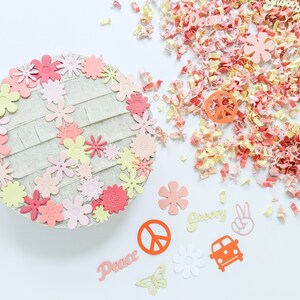May include: A peace sign made of felt with pink, yellow, and orange flowers around the edges. The peace sign is surrounded by confetti and other paper cutouts, including the words "Peace" and "Groovy", a peace sign, a butterfly, and a car.