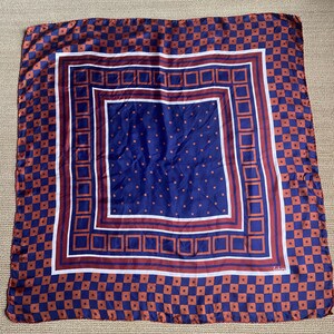 May include: A blue and brown silk scarf with a checkered pattern and a smaller square in the center with a polka dot pattern. The scarf has a white border and the text "Lehon" in the bottom right corner.