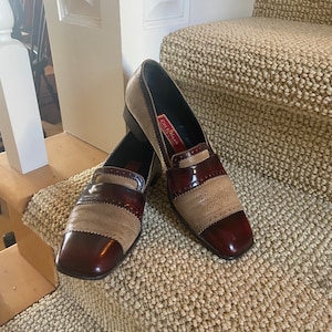 May include: A pair of brown and beige leather loafers with a decorative stitch detail. The loafers have a pointed toe and a low heel. The brand name "Cole Haan" is visible on the side of one loafer.