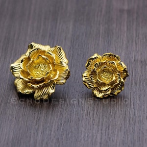 May include: A pair of gold-colored flower-shaped earrings. The earrings are made of metal and have a detailed design.